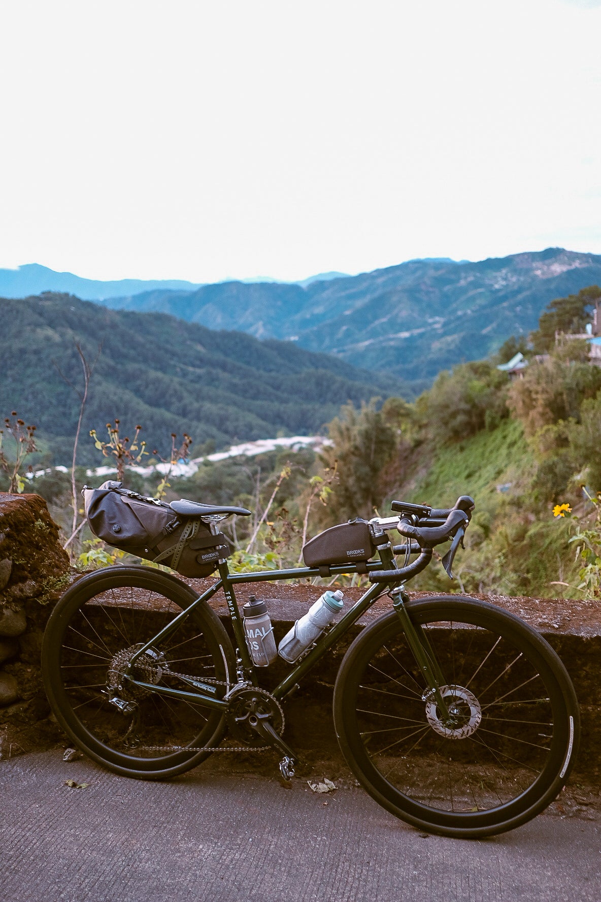 Bicycle with gear leaning against a stone wall with a scenic mountain view in the background