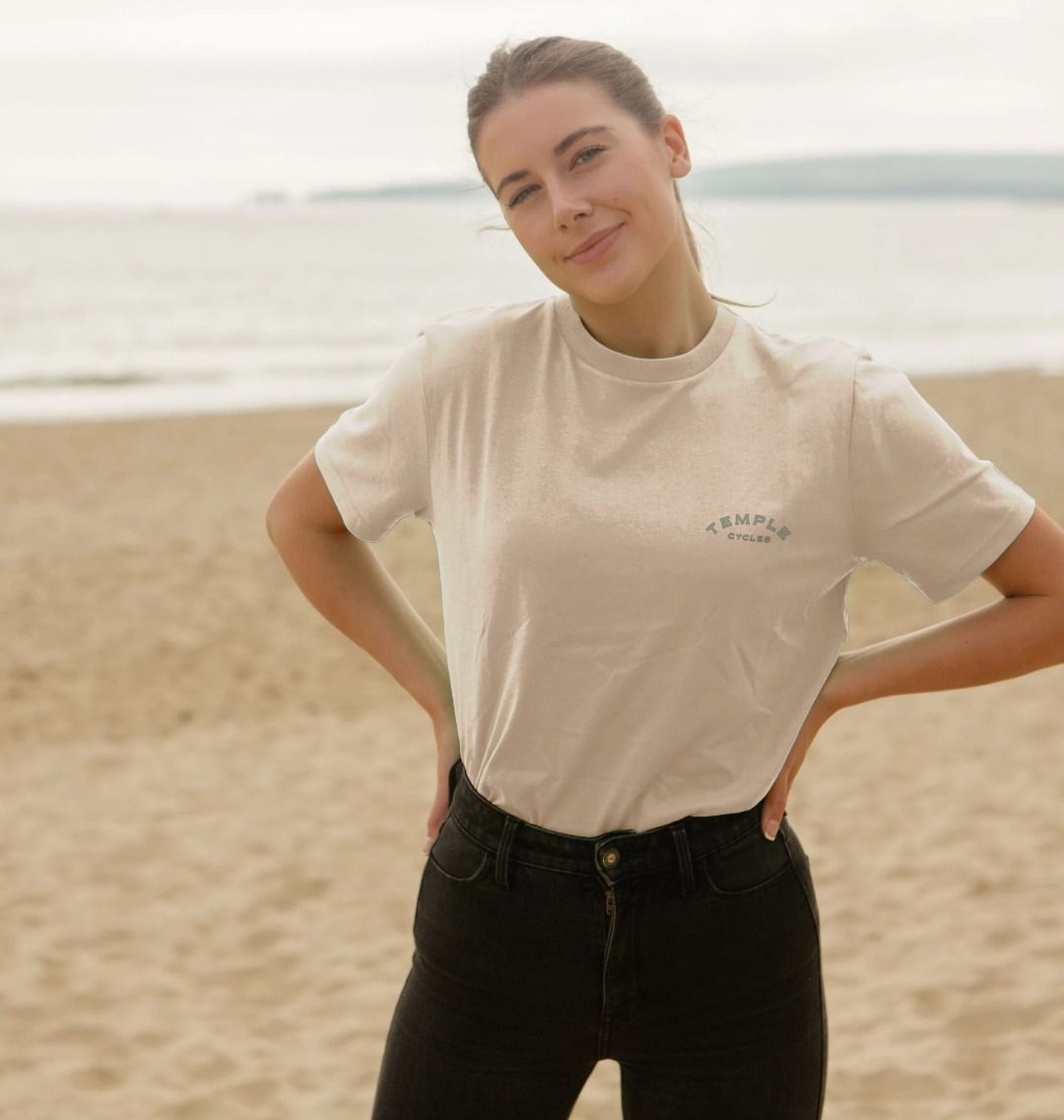 Model wearing Temple Cycles X Clara Jonas women’s graphic tee in cream, beach setting.