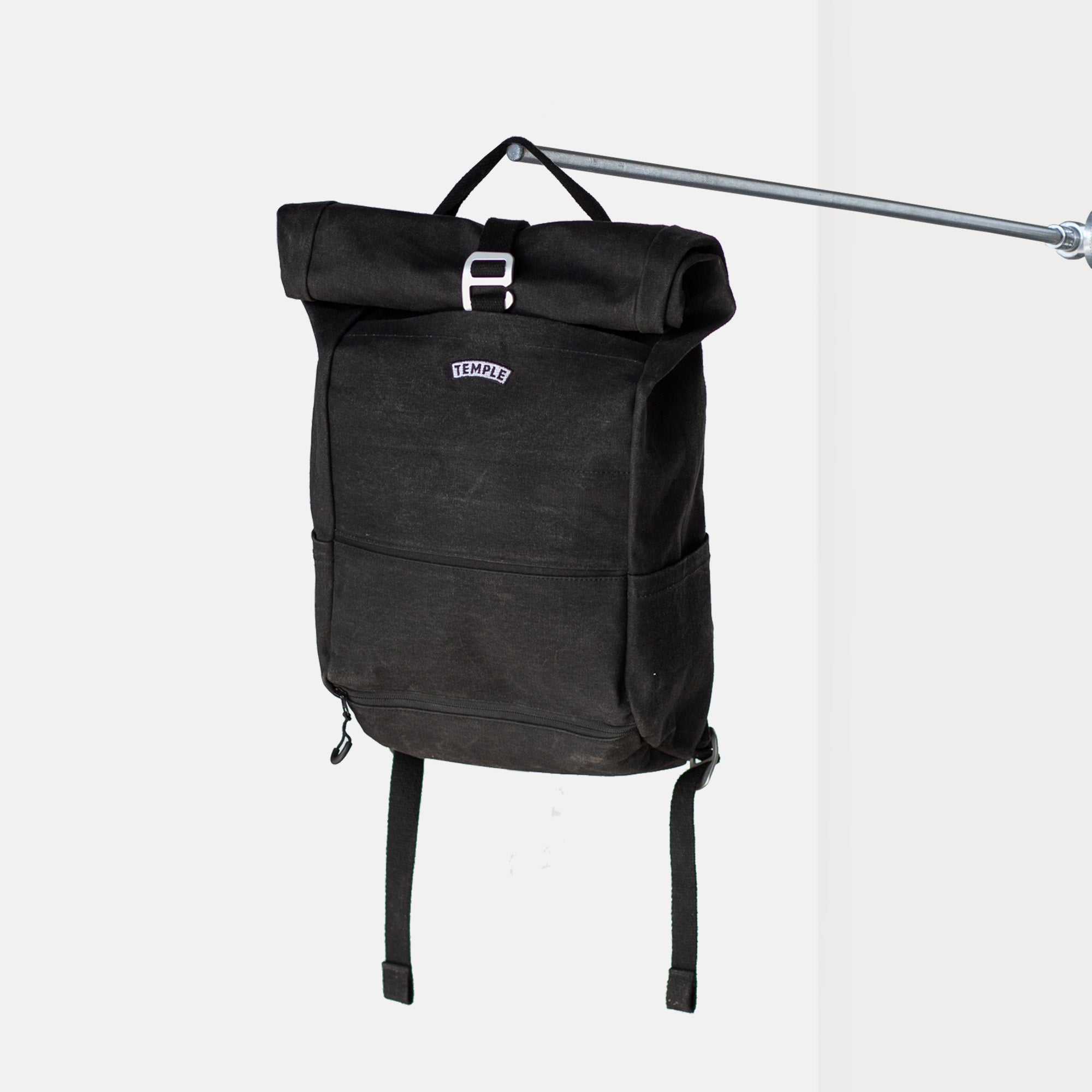 Black Temple Cycles canvas weather-proof pannier backpack secured with buckle fastening and padded straps hanging from a pole in a studio setting.