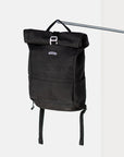 Black Temple Cycles canvas weather-proof pannier backpack secured with buckle fastening and padded straps hanging from a pole in a studio setting.