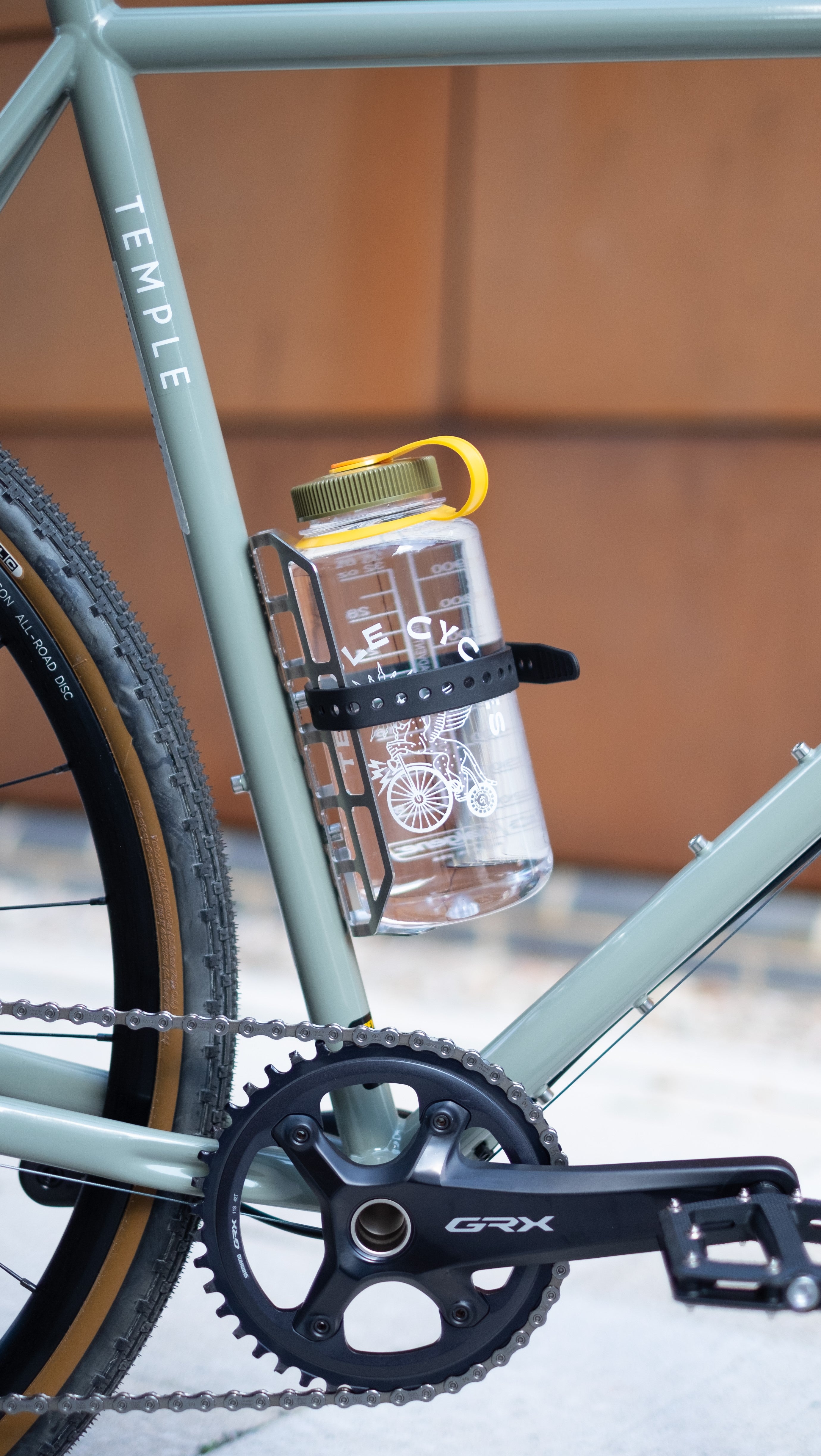 Adventure bike with GRX crankset and Nalgene bottle mounted in a cargo cage on the down tube, secured with a Voile strap.