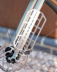 Cargo cage mounted to fork eyelets on an adventure bike with disc brakes and tan wall tyres.