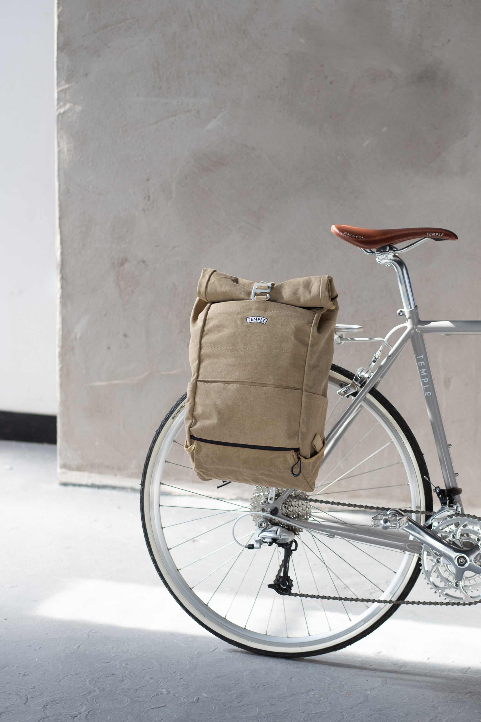 Beige roll-top backpack on rear pannier bike rack, urban setting.