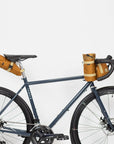 Three orange waterproof cycling bags attached to a navy road bike, studio setting.