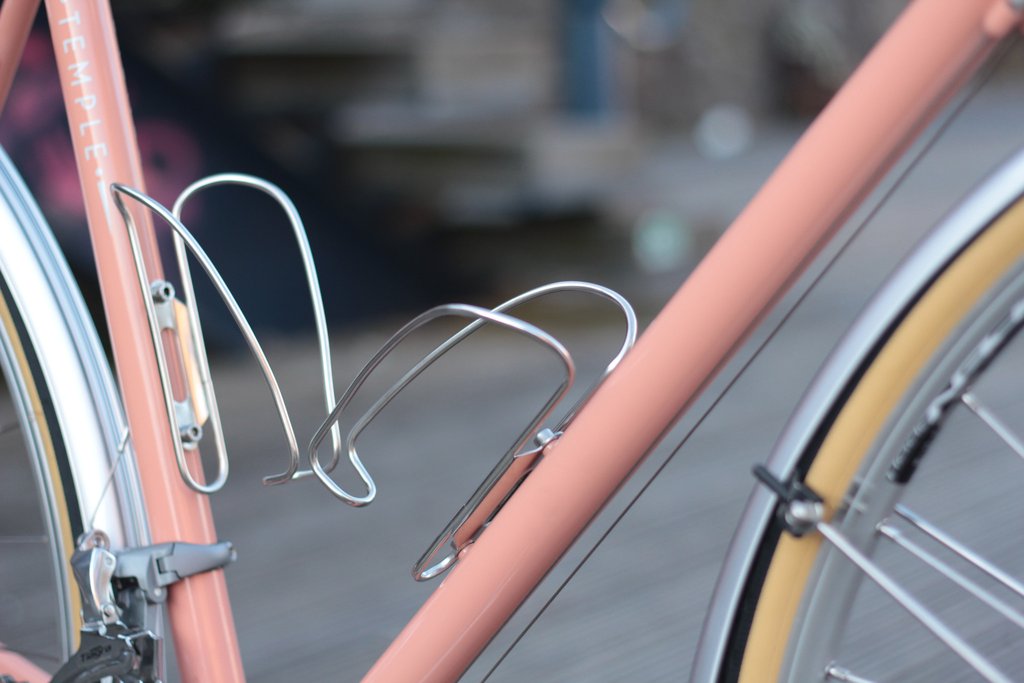 Pair of stainless steel bottle cages mounted on a pink Temple Cycles bike.