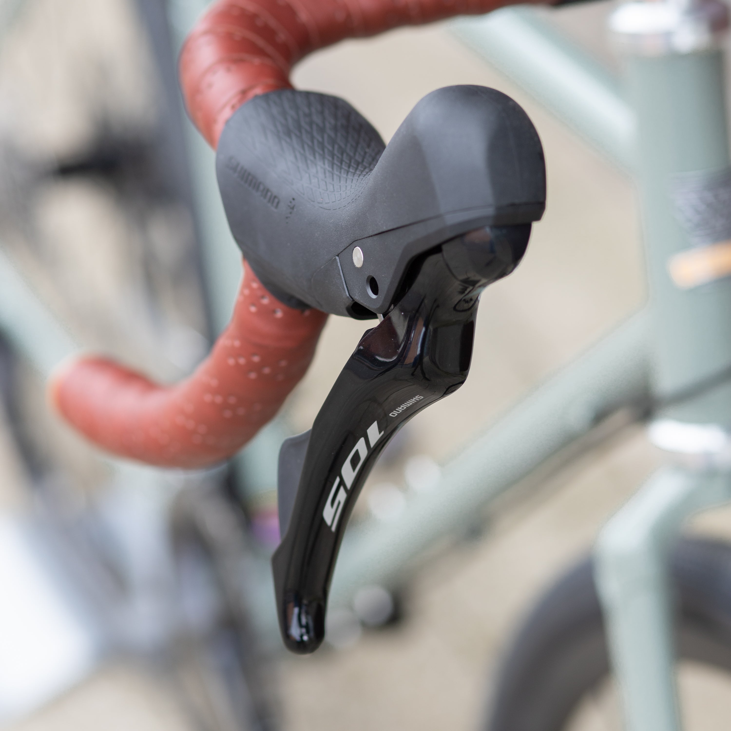 Shimano 105 brake lever on the left, leather-wrapped, flared handlebar of a gravel touring bike.