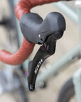 Shimano 105 brake lever on the left, leather-wrapped, flared handlebar of a gravel touring bike.