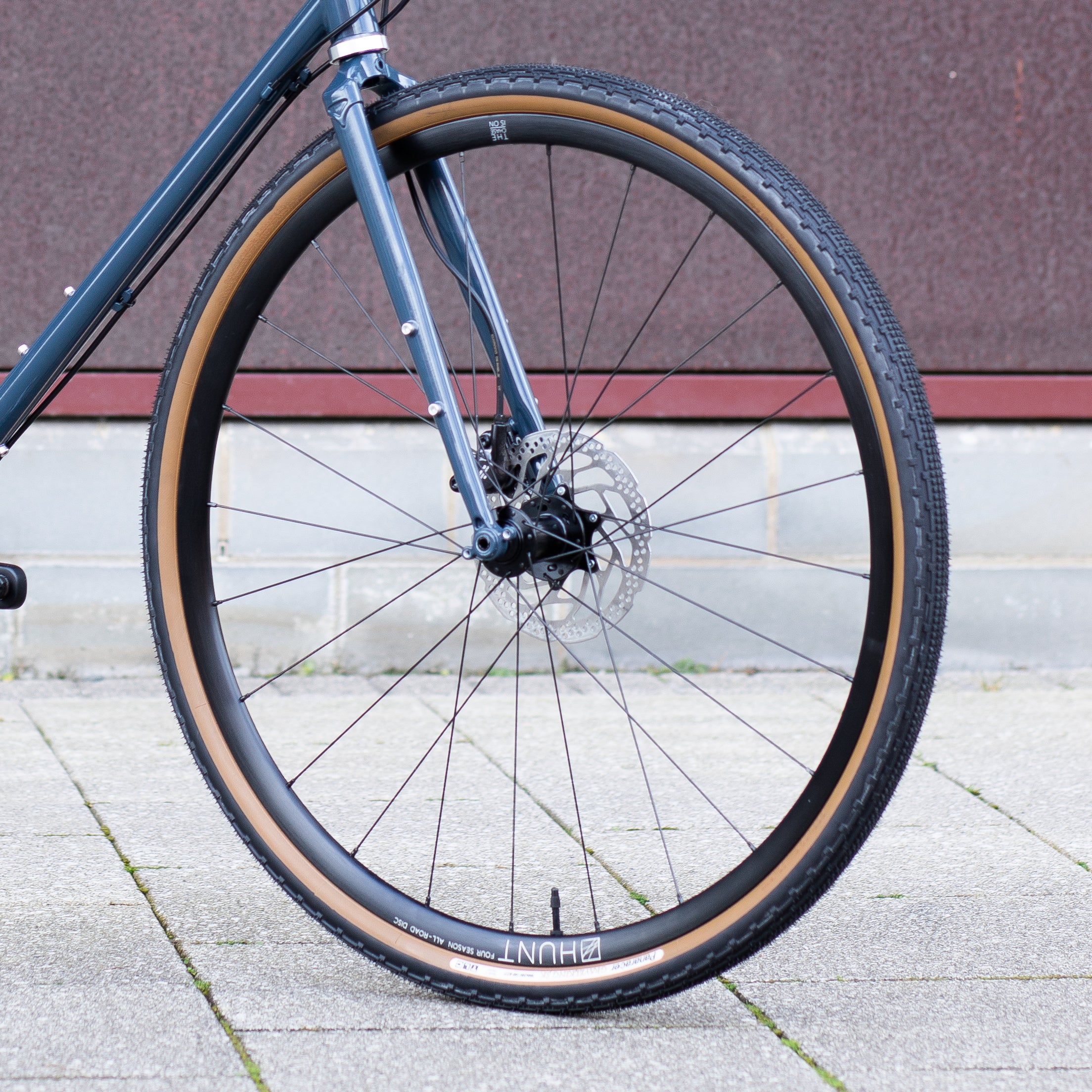 Front wheel hand built by Hunt | Tubeless Panaracer tyre on blue steel gravel bike in an urban setting.