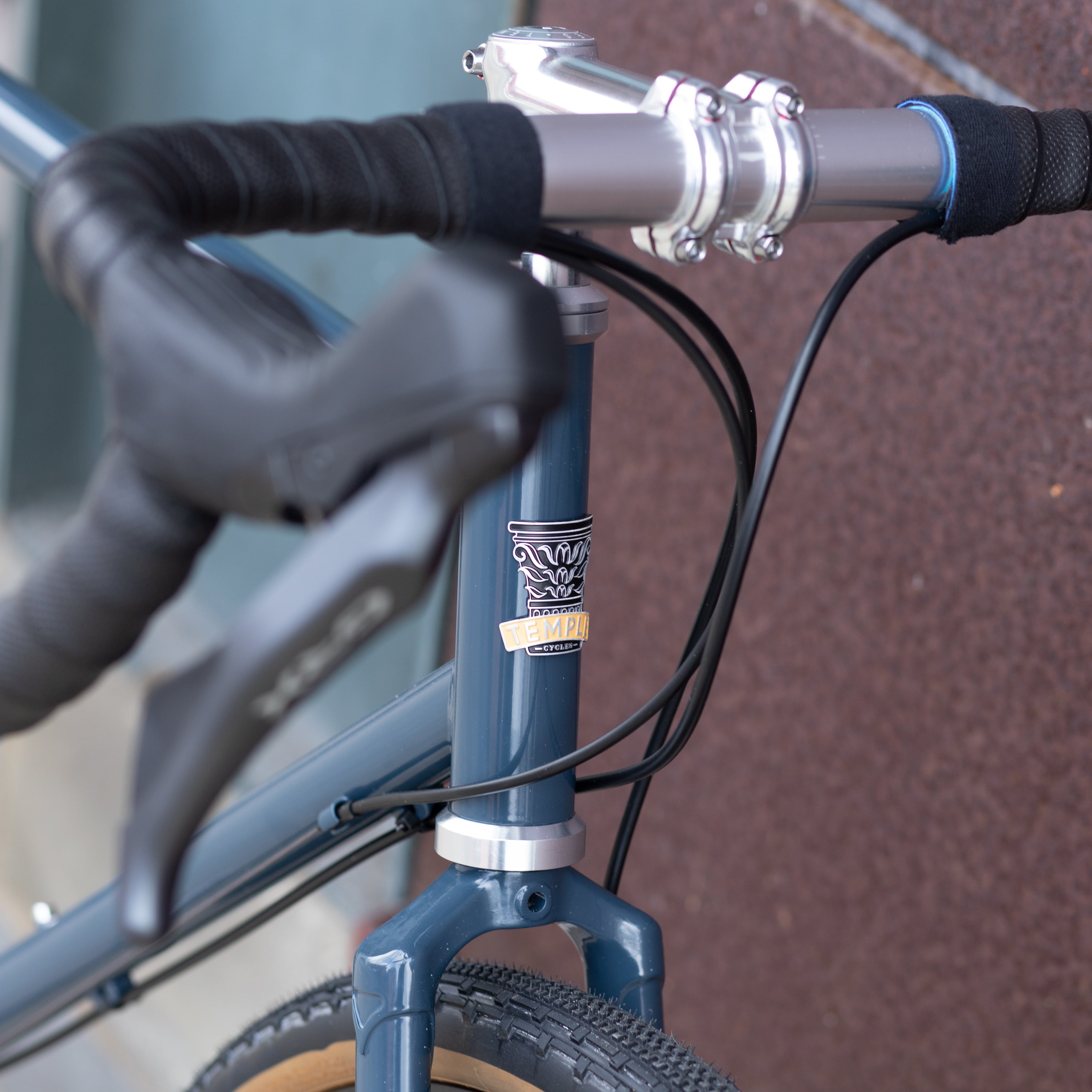 Temple handmade head badge beneath flared handlebars on a blue, steel, gravel bike.