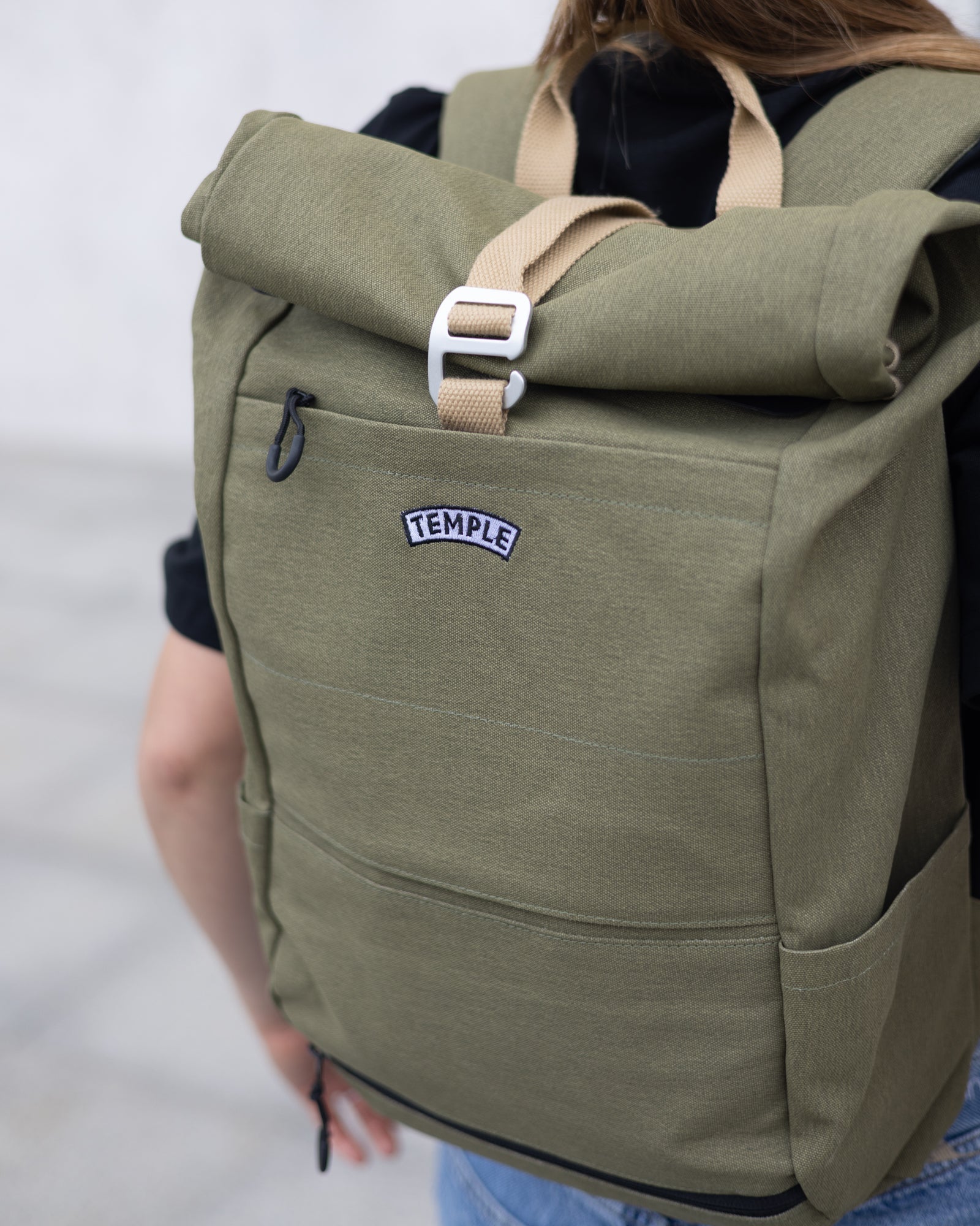 Close up of a person wearing a Temple Cycles weather-proof pannier roll-top backpack in olive green.