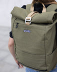 Close up of a person wearing a Temple Cycles weather-proof pannier roll-top backpack in olive green.