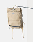 Waterproof beige roll-top canvas pannier backpack hanging on a pole in a studio setting.
