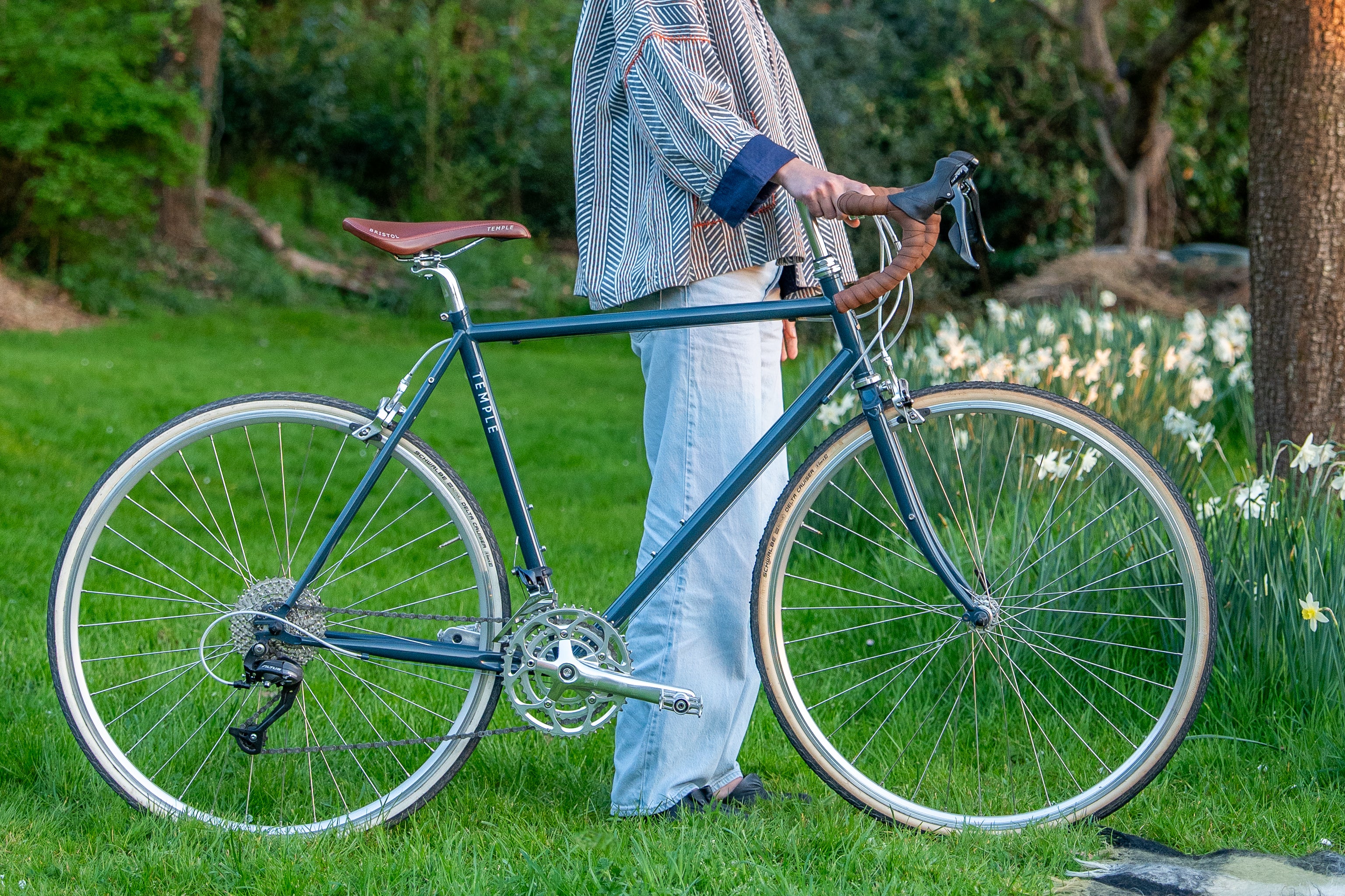 Model holding a steel framed classic tour bike in navy blue stood in a rural setting.