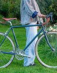 Model holding a steel framed classic tour bike in navy blue stood in a rural setting.