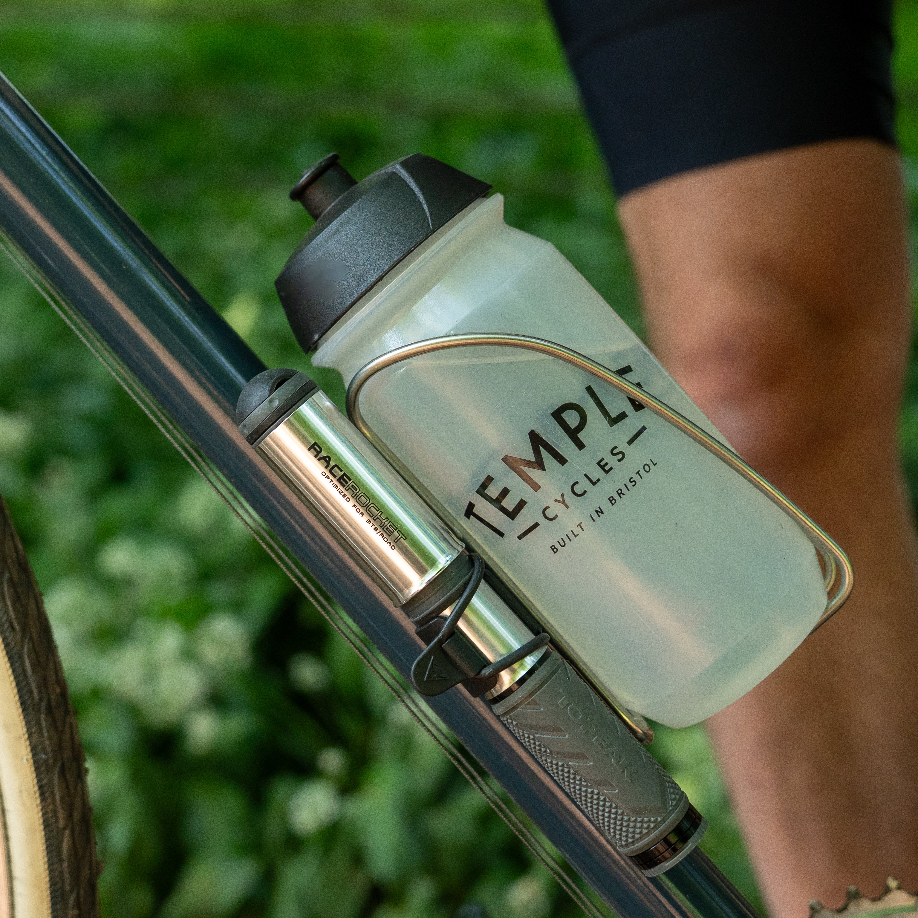 A Temple Cycles water bottle mounted on a bike frame in a steel water bottle cage with a mini pump.