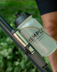 A Temple Cycles water bottle mounted on a bike frame in a steel water bottle cage with a mini pump.