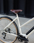 Rear wheel, with wide-ranging Shimano gears on a minimalist cream electric bicycle.