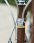 Front-on close up shot of a Temple Cycles badge on a brown steel framed bike.