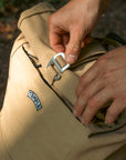 Hands fastening the buckle on a Temple canvas backpack in Sandstone.