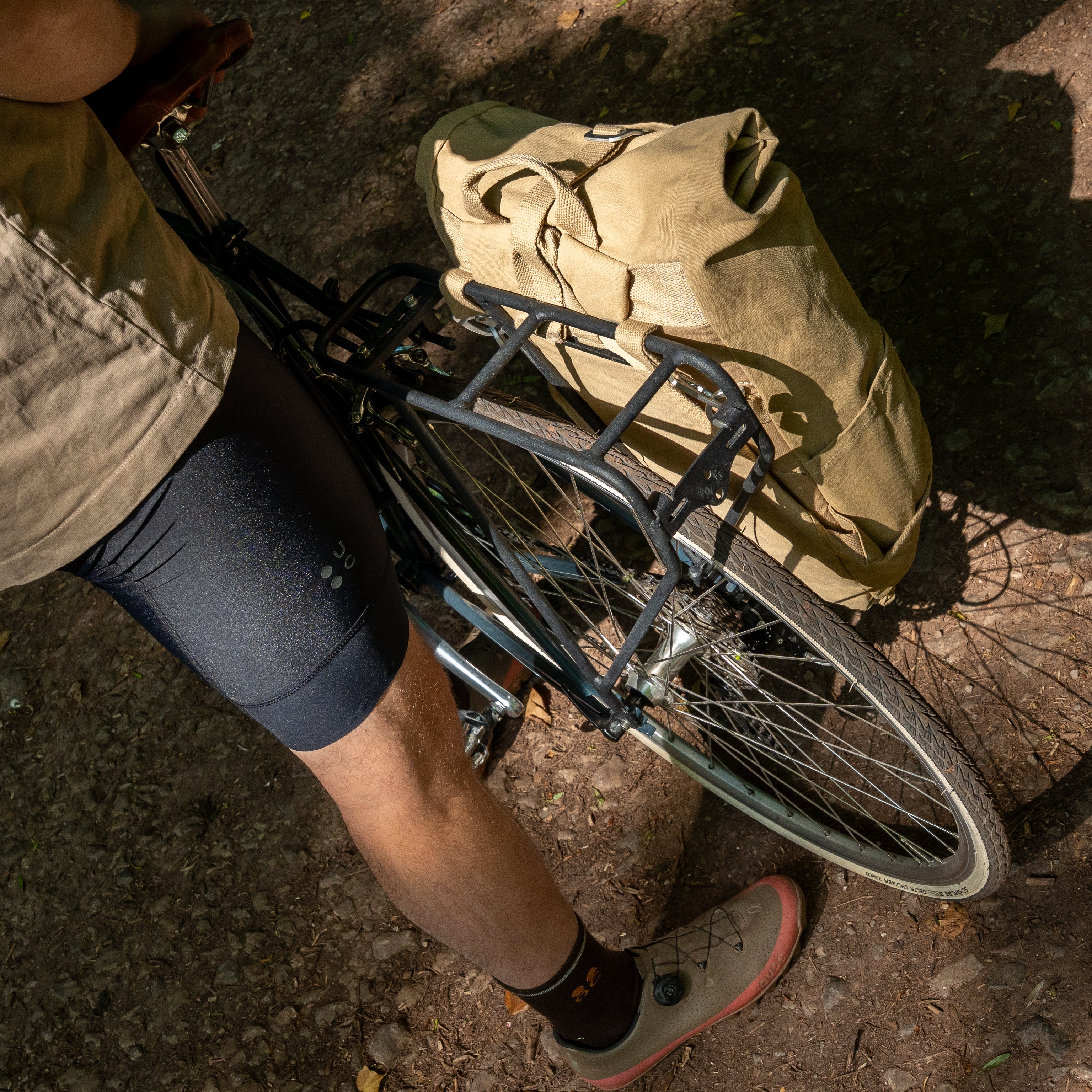 Cyclist standing beside a bicycle fitted with a beige pannier backpack secured to a black rear rack.
