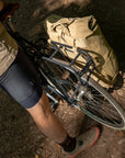 Cyclist standing beside a bicycle fitted with a beige pannier backpack secured to a black rear rack.
