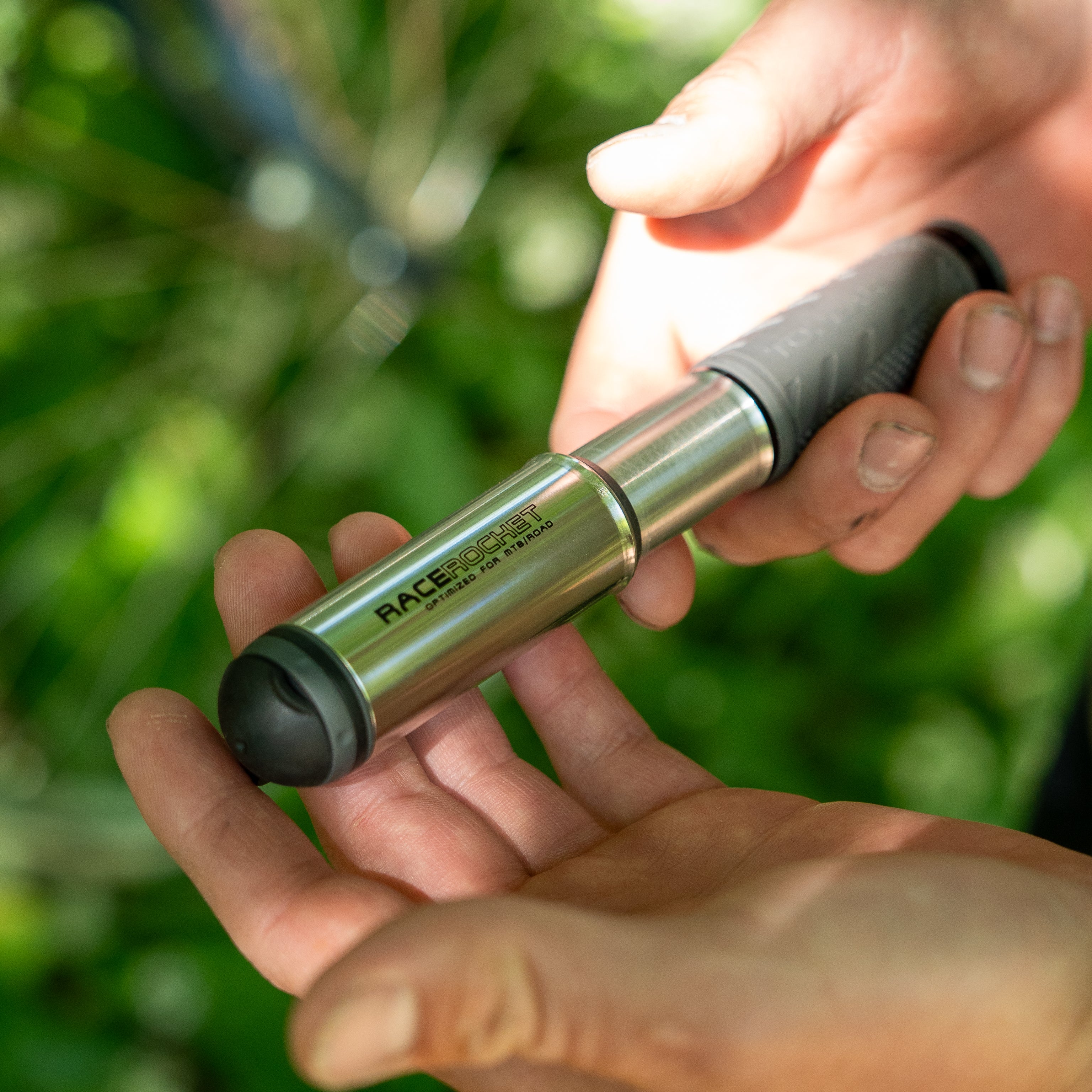Hands holding a compact silver bicycle mini pump.