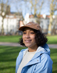 Model wearing simple, embroidered brown cap made from 100% cotton, park setting.