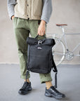 Model holding casual men’s black backpack, urban setting.