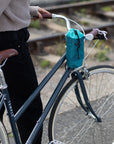 Model holding step through steel bike with a women’s green snack bag, urban setting.