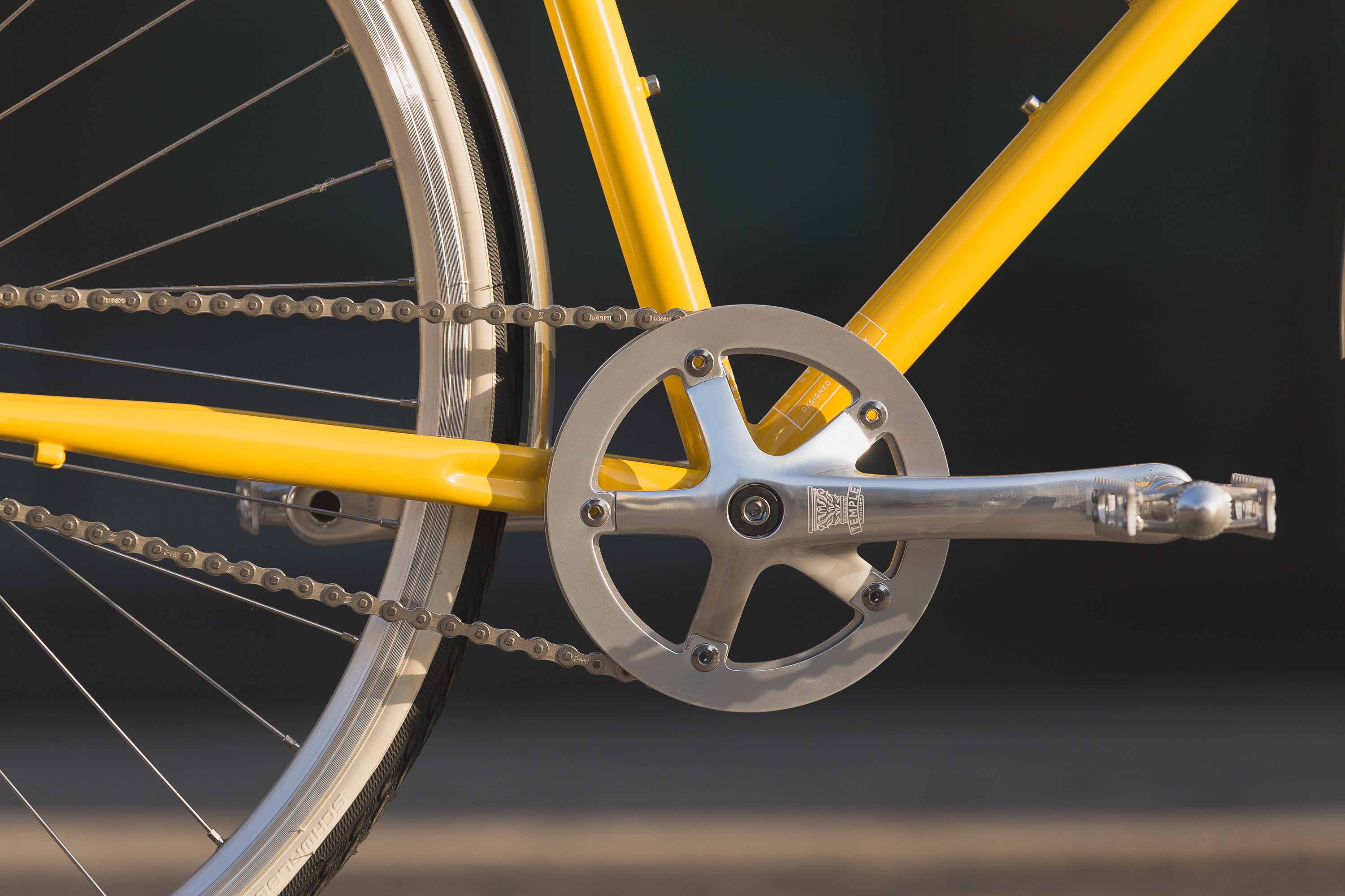 Traditional alloy pedals and Shimano chain on a yellow lightweight city bike.
