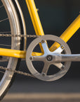 Traditional alloy pedals and Shimano chain on a yellow lightweight city bike.