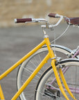 Two lightweight daily commuting bikes in yellow and pink, urban setting.