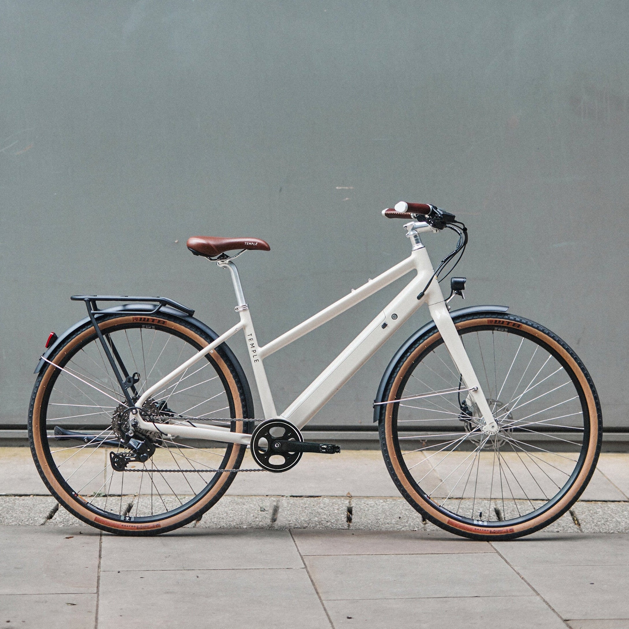 White bicycle with brown seat and tires against a gray wall