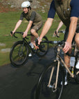 Two cyclists riding fast, functional steel road bikes in a rural setting. 