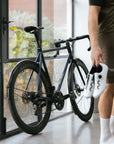 Model standing next to lightweight durable road bike, in-door setting.