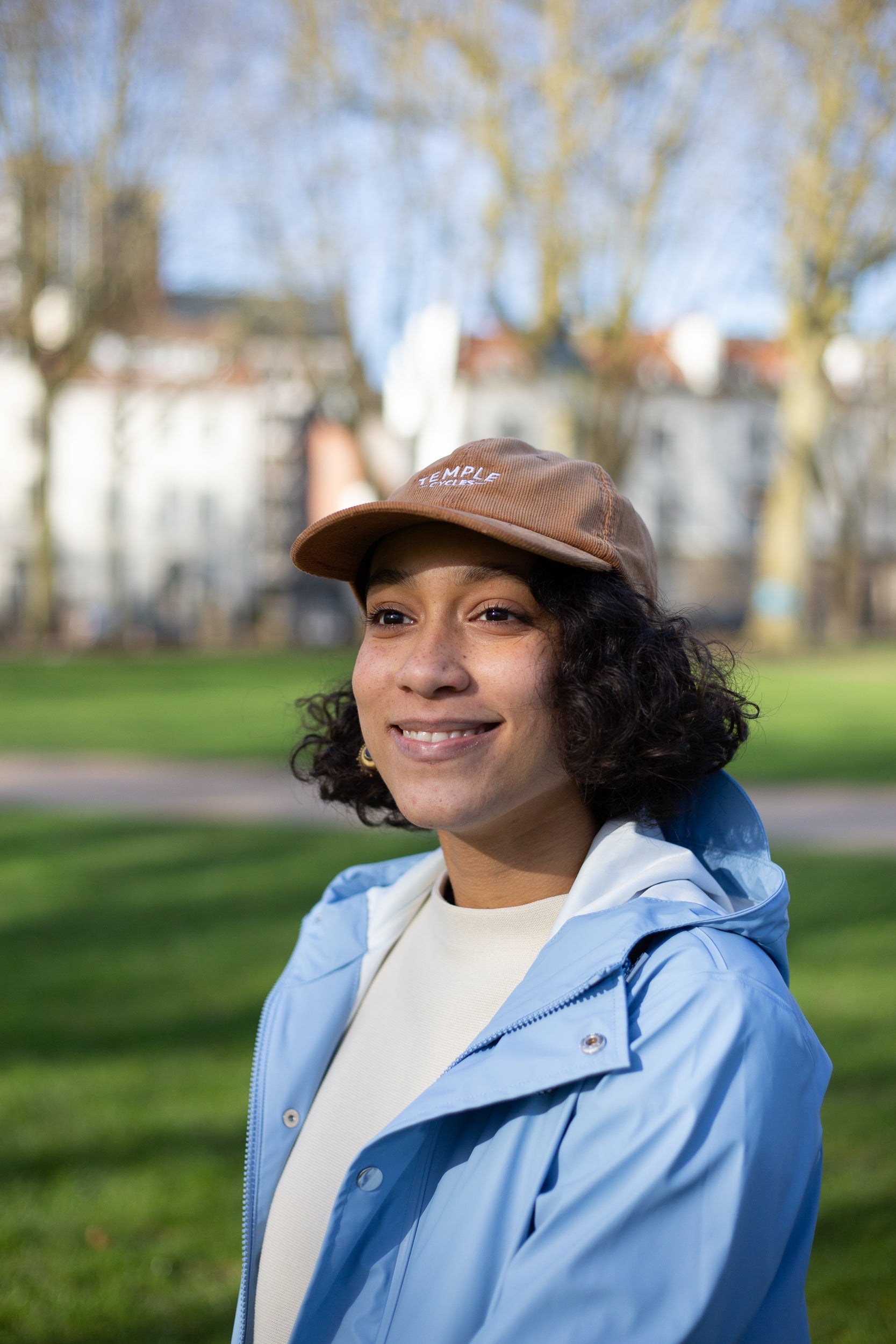 Model wearing simple, embroidered brown cap made from 100% cotton, park setting. 