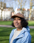 Model wearing simple, embroidered brown cap made from 100% cotton, park setting. 