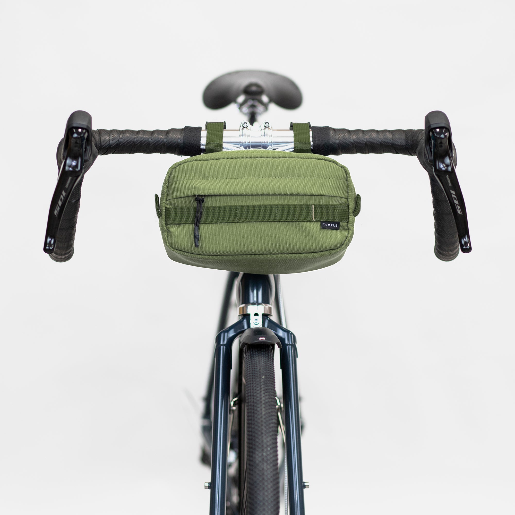 Green waterproof bar bag attached with magnetic fastenings to handlebars, studio setting.