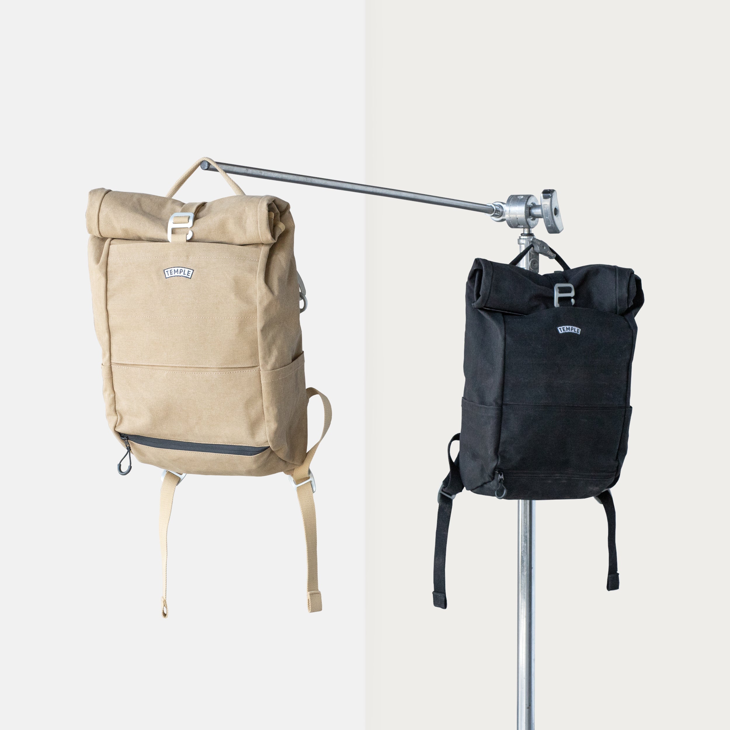 Two Pannier, roll-top backpacks in black and beige, studio setting.