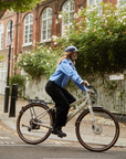 Person riding a bicycle on a city street with a brick building and trees in the background
