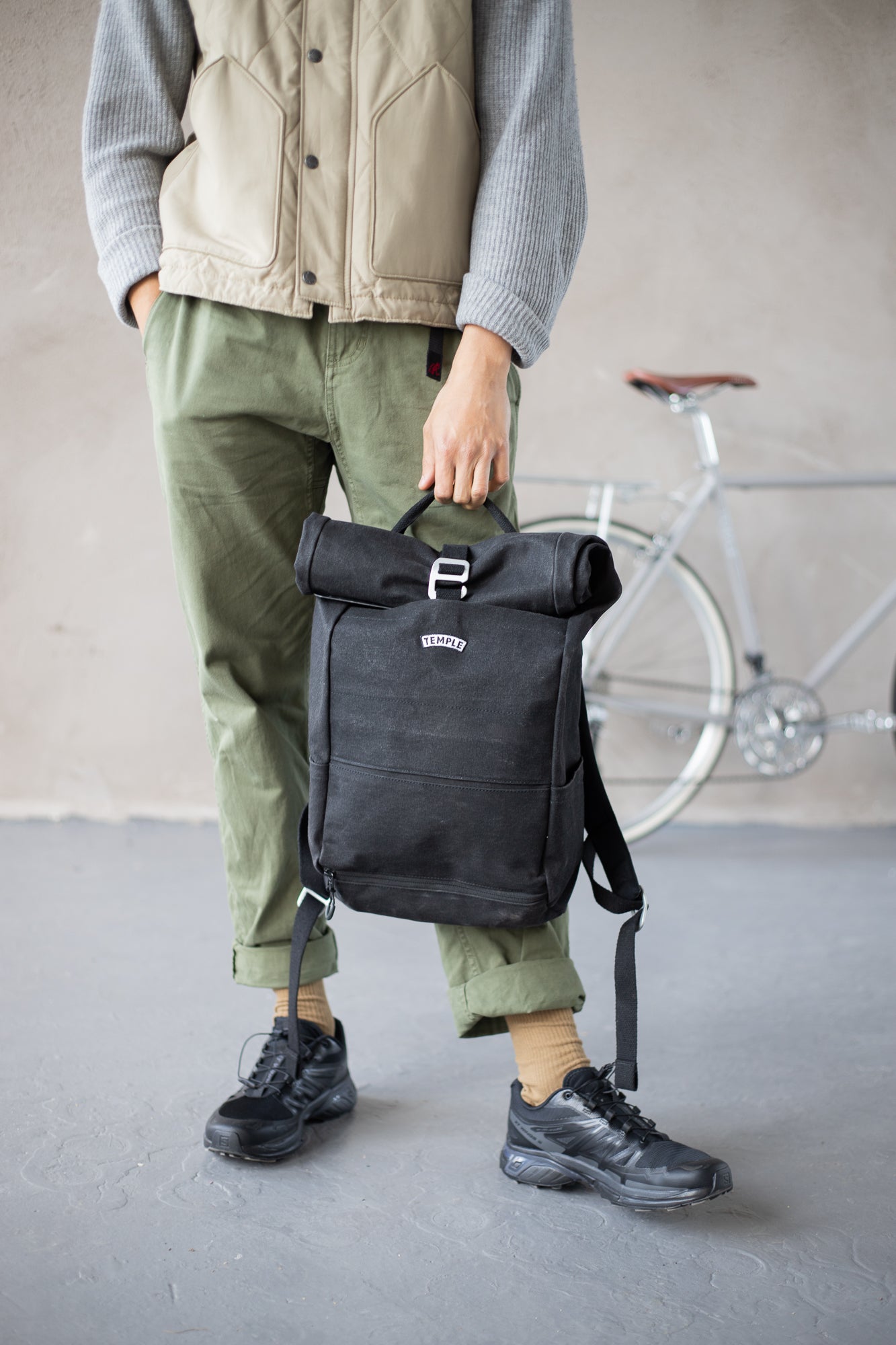 Model holding casual men’s black backpack, urban setting. 