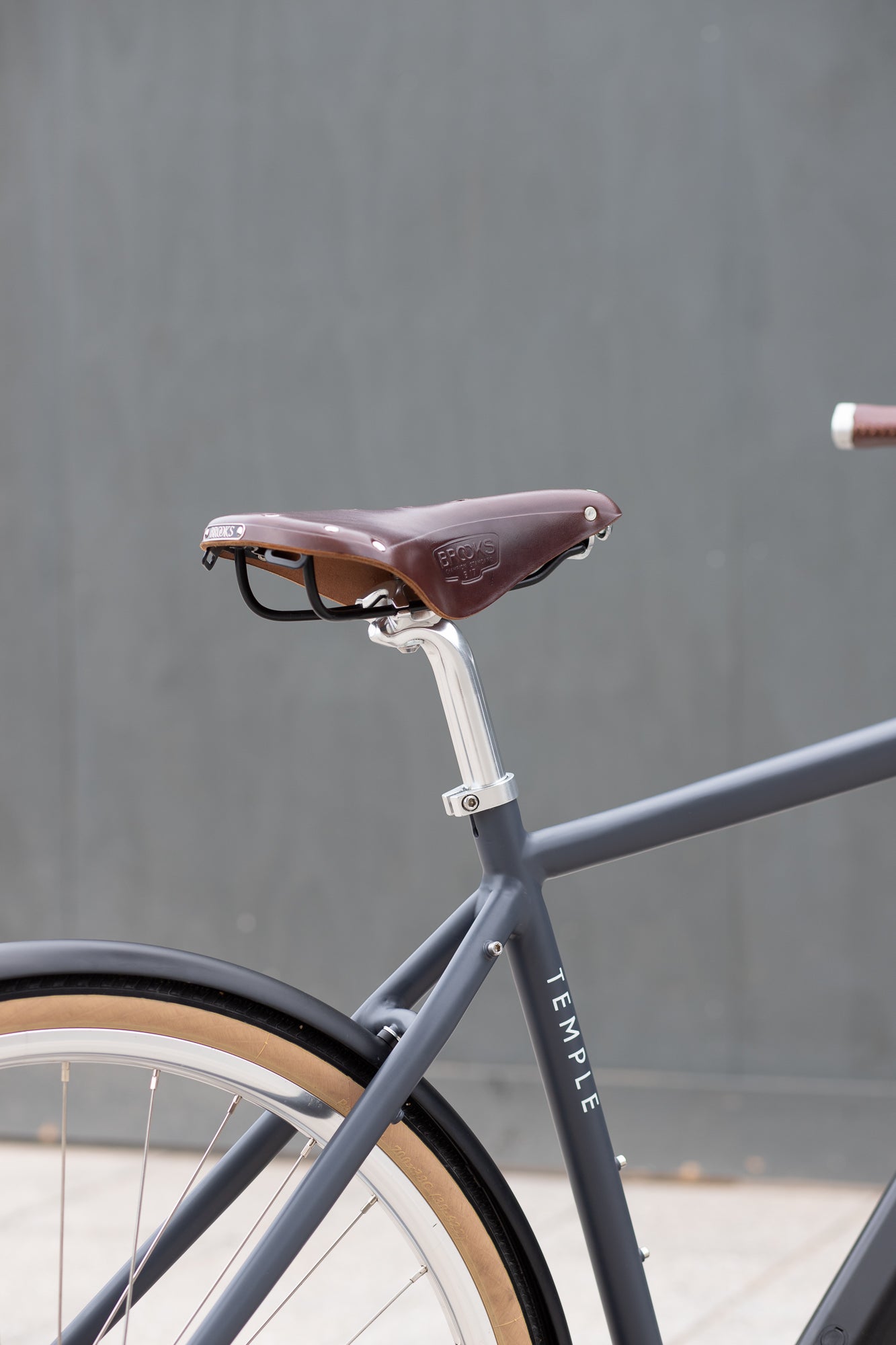 Minimalist black e-bike with Brooks leather saddle, urban setting. 