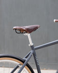 Minimalist black e-bike with Brooks leather saddle, urban setting. 