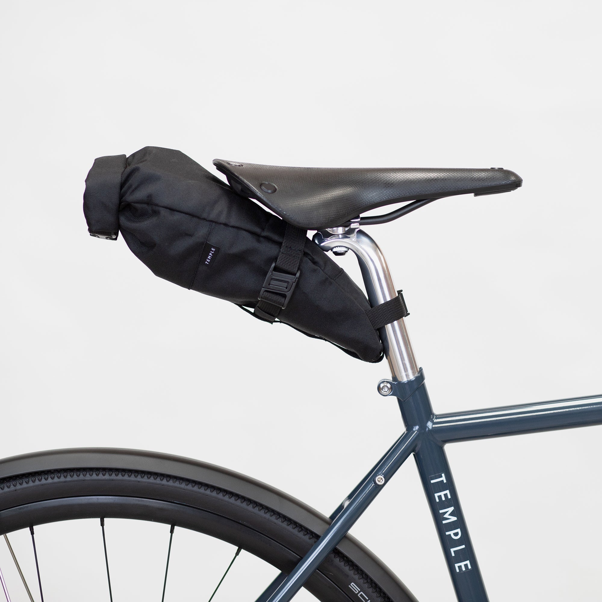 Black waterproof saddle bag attached to a gravel bike, studio setting.