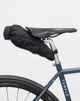 Black waterproof saddle bag attached to a gravel bike, studio setting.