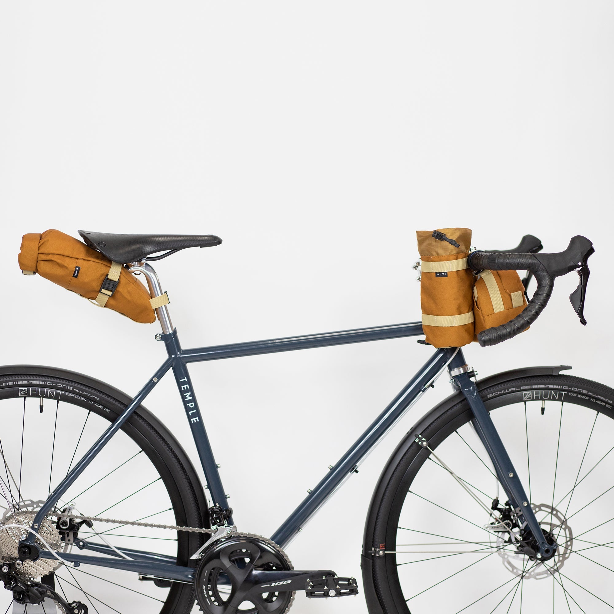 Orange roll-top small bike bags attached to a navy adventure bicycle, studio setting.