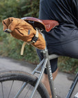 Orange roll-top bike bag attached to leather saddle, rural setting.