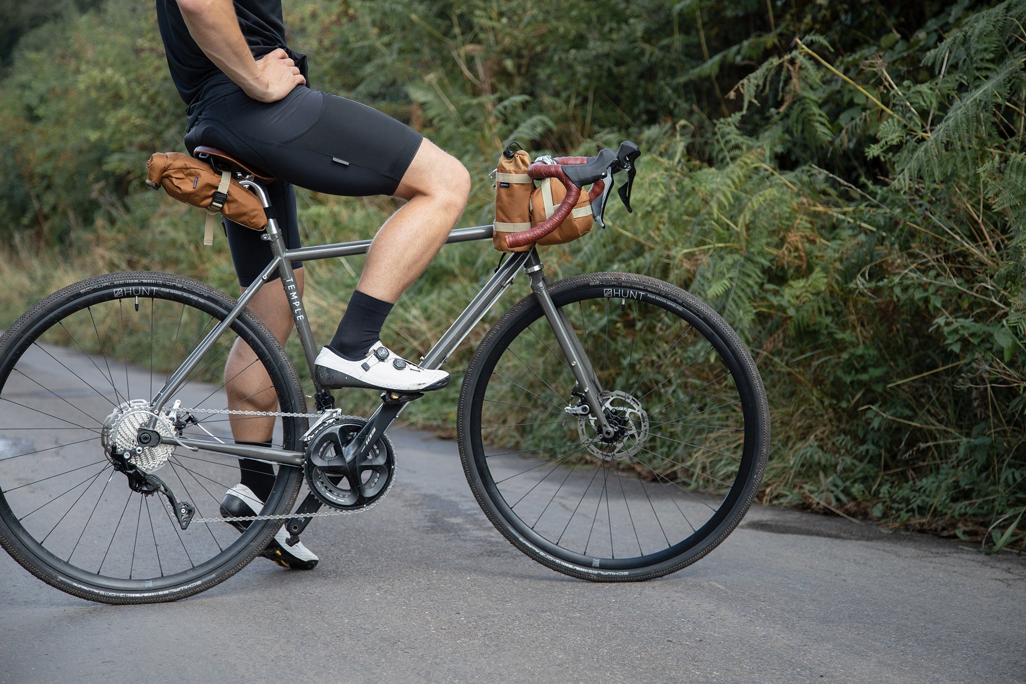 Model perched on a gravel bike with three orange, durable bike bags attached, rural setting.