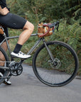 Model perched on a gravel bike with three orange, durable bike bags attached, rural setting.