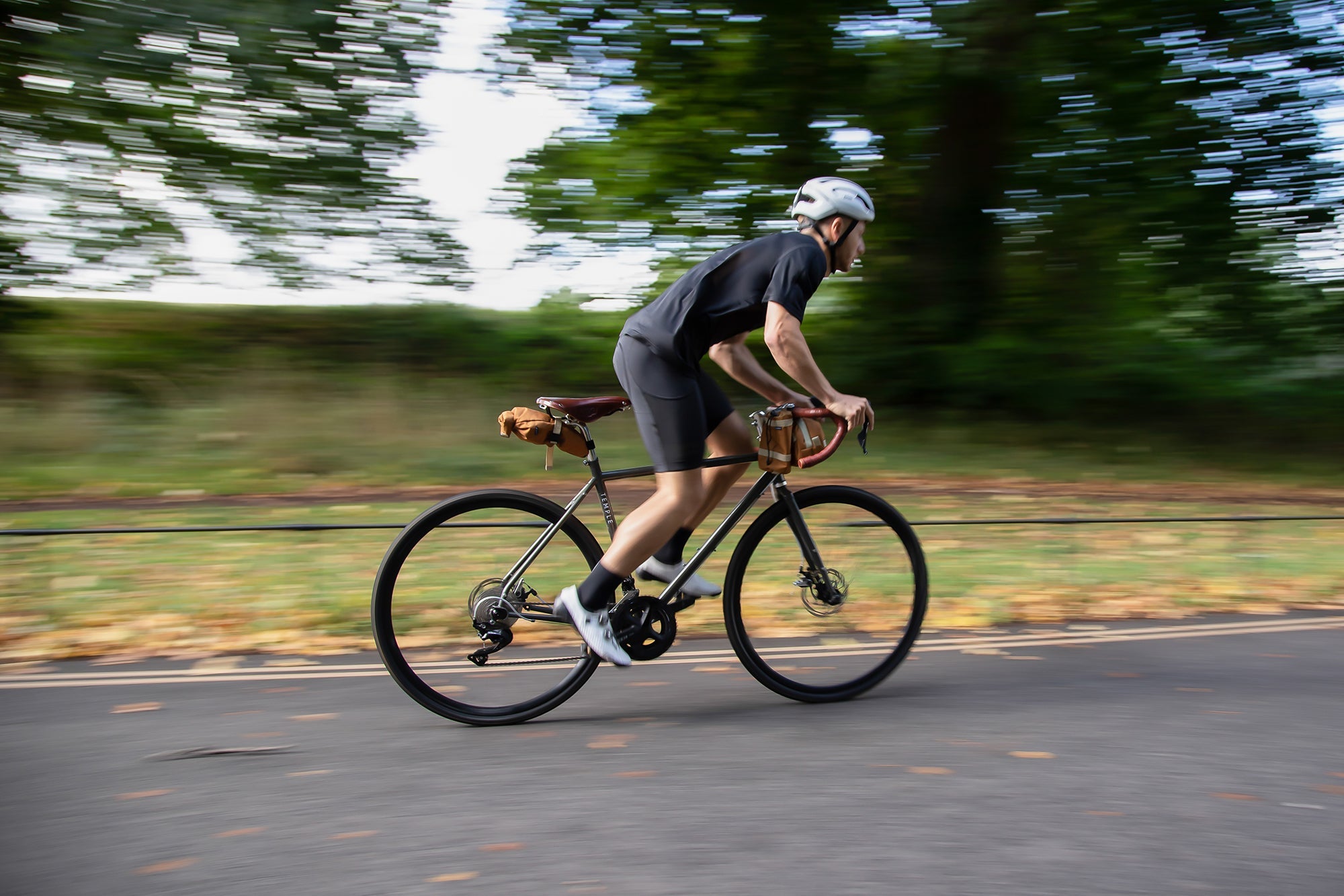 Model cycling on a bikepacking tour with three orange bicycle bags attached.